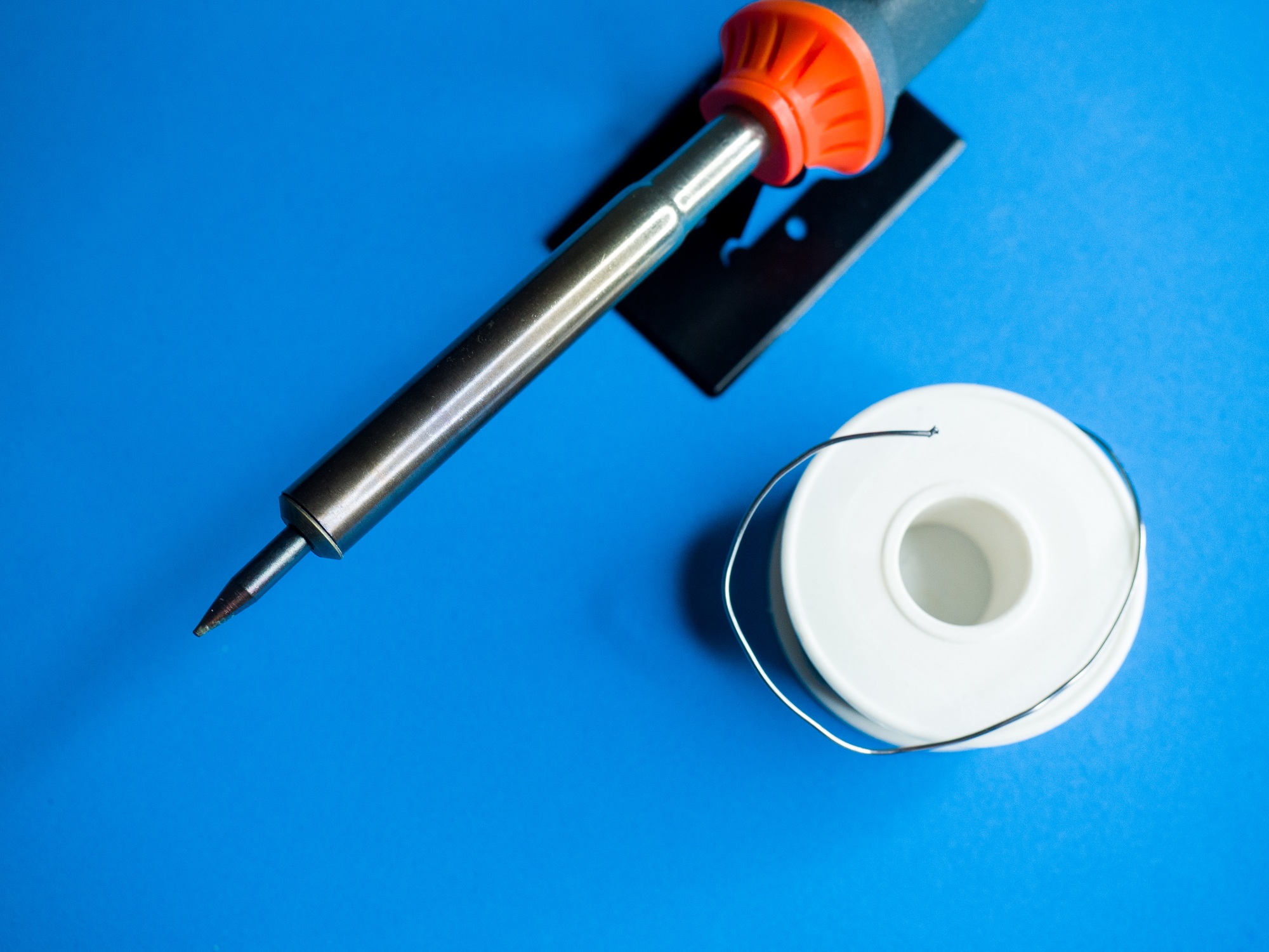 Tin soldering iron tool with a tin roll on a blue surface