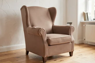 Housse extensible taupe ajustée sur un fauteuil à oreilles dans un salon scandinave, avec échantillon de tissu jersey-spandex sur l'accoudoir